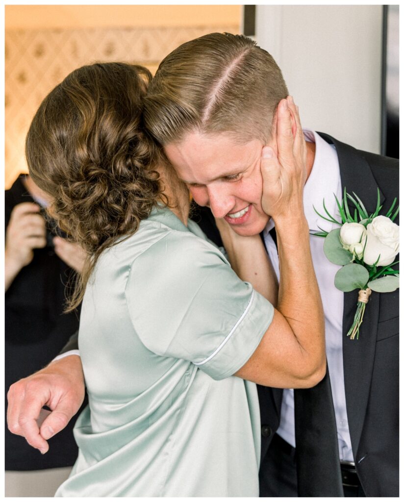 Bride's mom embracing groom after attaching his boutonnière floral decoration 